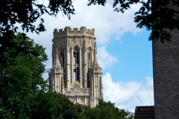 The University of Bristol Wills Memorial Building framed by leaves against a blue sky, as seen from the nearby Cabot Tower.